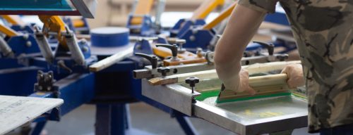 Worker and Serigraphy silk screen print process at clothes factory.